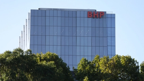 BHP corporate headquarters building with a large red BHP sign on a glass office tower above green trees