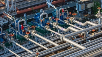 Aerial view of industrial pipework with orange valve wheels and blue pump units at a processing plant